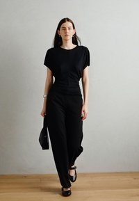 Must väljakujundusega must lühikeste käistega topp koos mustade laiadest pükstest. Omab elegantset siluetti ja lihtsaid aksessuaare.