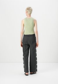 Light green sleeveless top paired with gray wide-leg pants, featuring embroidered palm tree accents along the sides. Flat shoes visible.