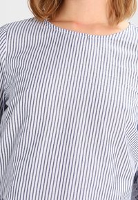 Maglietta a righe bianca e blu navy, con scollatura rotonda, maniche corte e tessuto leggero dalla texture liscia.