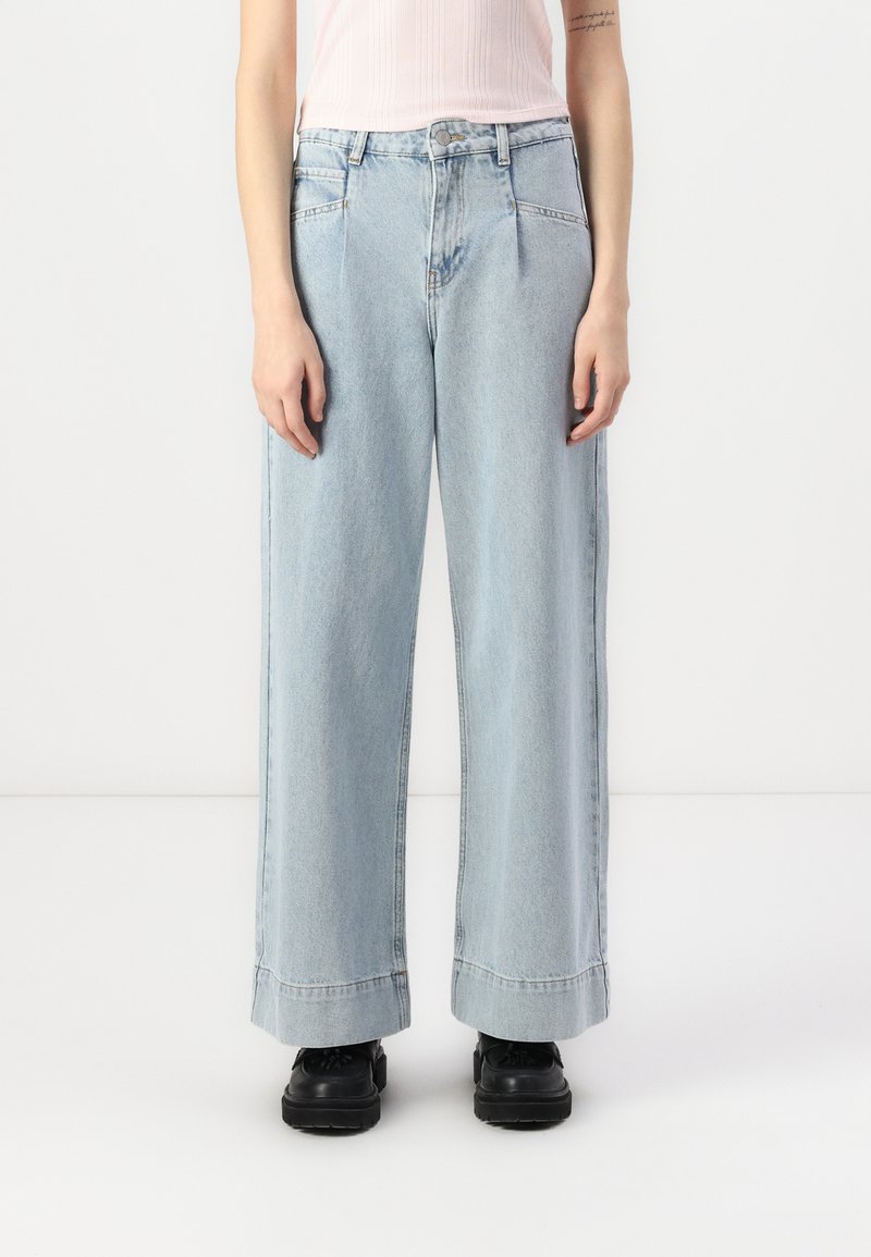 Svijetloplave široke traperice s visokim strukom, s prednjim gumbom i dva bočna džepa. Suptilna izblijedjela tekstura, minimalno šivanje.