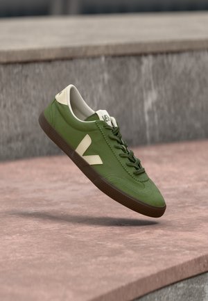 Zeleni sneaker od platna s kremastom petnom kapicom i velikim kremastim logotipom "V" sa strane. Ima teksturiranu smeđu gumenjaču.