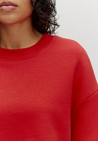 Rode sweatshirt met een geribbelde ronde halslijn, voorzien van een gladde textuur en een losse pasvorm. Er zijn geen zichtbare patronen of accenten.