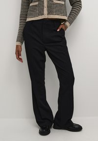 Sorte, skræddersyede bukser med løs pasform og sidelommer, lavet af et glat stof. Kombineret med en mønstret, cropped cardigan.
