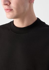 T-shirt nera in cotone a girocollo con texture liscia e colletto a coste, arricchita da dettagli di cucitura sottili lungo il scollo.