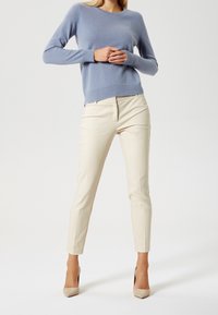 Pull bleu clair à manches longues, décolleté rond, assorti à un pantalon crème fuselé et des escarpins nude. Texture lisse, design minimaliste.