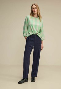 Zielono-beżowy sweter w kratkę z bufiastymi rękawami, połączony z granatowymi spodniami straight-leg z dwoma guzikami, noszony z czarnymi butami.