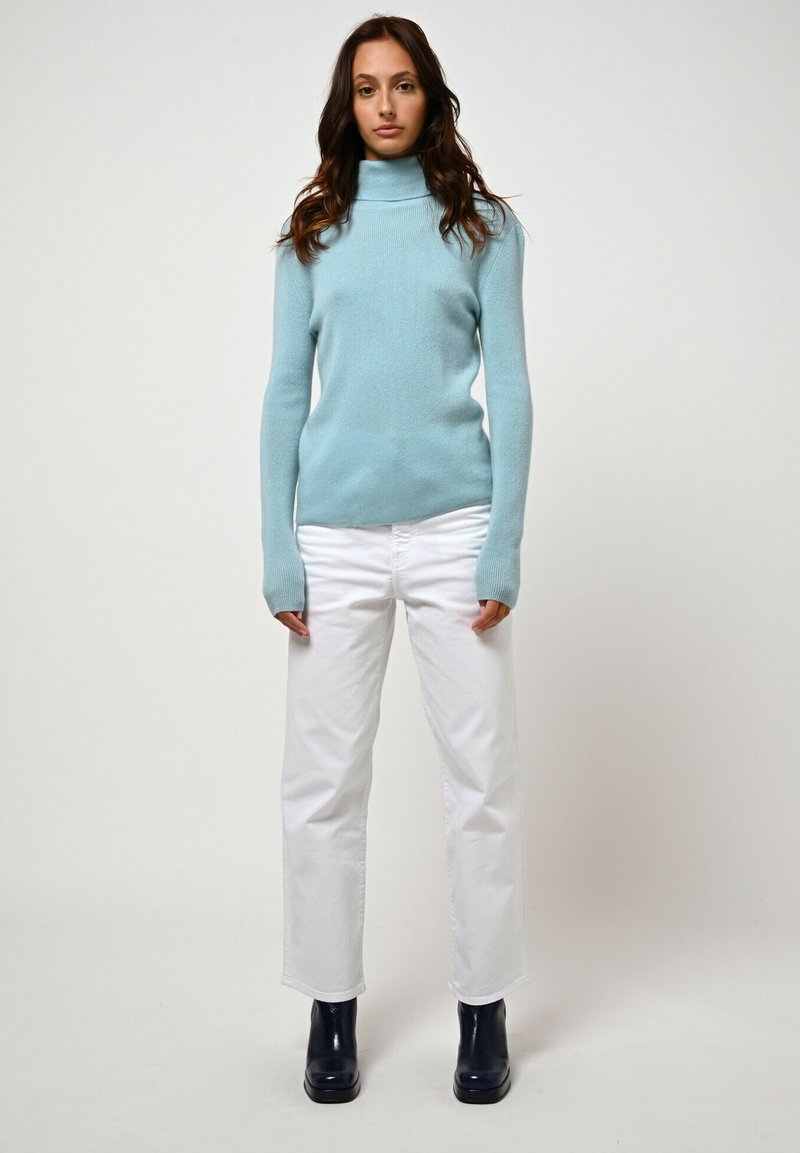 Hellblauer Rollkragenpullover aus weichem Strickmaterial, kombiniert mit weißen Jeans im geraden Schnitt und dunklen Stiefeletten. Einfaches und figurbetontes Design.