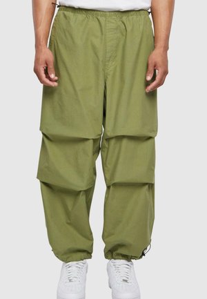 Pantalones cargo verdes con cintura elástica, que cuentan con múltiples bolsillos grandes y puños fruncidos. Combinados con zapatillas blancas.