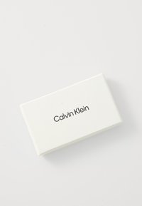 Balts taisnstūra kaste ar gludu faktūru, uz kuras ir uzraksts "Calvin Klein" treknā, mūsdienīgā fontā. Minimālisma dizains bez papildu rotājumiem.