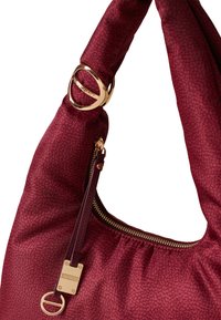Burgundy shoulder bag with textured fabric, gold metal hardware, and a zippered pocket featuring a branded tag and key ring detail.