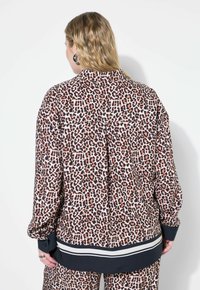Leopardenmuster-Hemd mit langen Ärmeln, Knopfmanschetten und einem kontrastierenden schwarz-weiß gestreiften Saum. Glattes Material und lockere Passform.