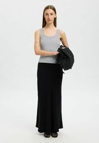 Débardeur gris à côtes, jupe maxi noire, tenant un sac tissé noir. Le débardeur a une encolure dégagée ; la jupe présente un design lisse et fluide.