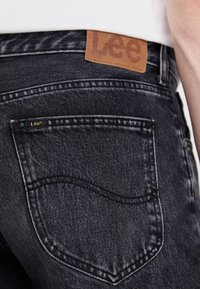 Mustad mustad teksased sisaldavad suurt tagumist taskut, millel on kuldne "Lee" logo. Vöökoht on kaunistatud pruuni nahkplaadiga.