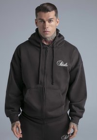 Svart zip-up hoodie i bomullsblandning med en känguruficka och huva med dragsko. Broderad logotyp på vänster bröst.