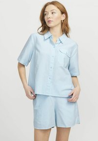 Camicia azzurra a maniche corte con bottoni frontali e taschino singolo, abbinata a pantaloni a righe coordinati, in morbido cotone.