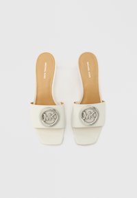 Bijele natikače sa širokom naramenicom na kojoj se nalazi srebrni okrugli logo. Glatka kožna tekstura i ravni, pravokutni potplat.