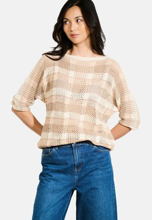 Lightweight, knitted sweater in beige with a checkered pattern, loose fit, and short sleeves. Paired with high-waisted blue jeans.