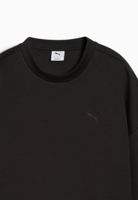 Camiseta de manga corta negra hecha de suave algodón, con cuello redondo y un logo bordado en tono sobre el lado izquierdo del pecho. Textura suave.