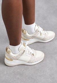 Sneakers bianchi con tomaia in tessuto beige a motivo, dettagli dorati e suola in gomma bianca. Presentano lacci classici e supporto per la caviglia imbottito.