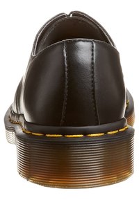 Tacco di scarpa in pelle nera con cuciture gialle e suola traslucida texturizzata, mostrato dal retro su sfondo bianco.