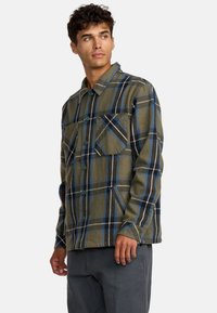 Camicia a quadri verdi con strisce blu e nere, chiusura con bottoni, due tasche anteriori, dal taglio morbido e tessuto soffice.