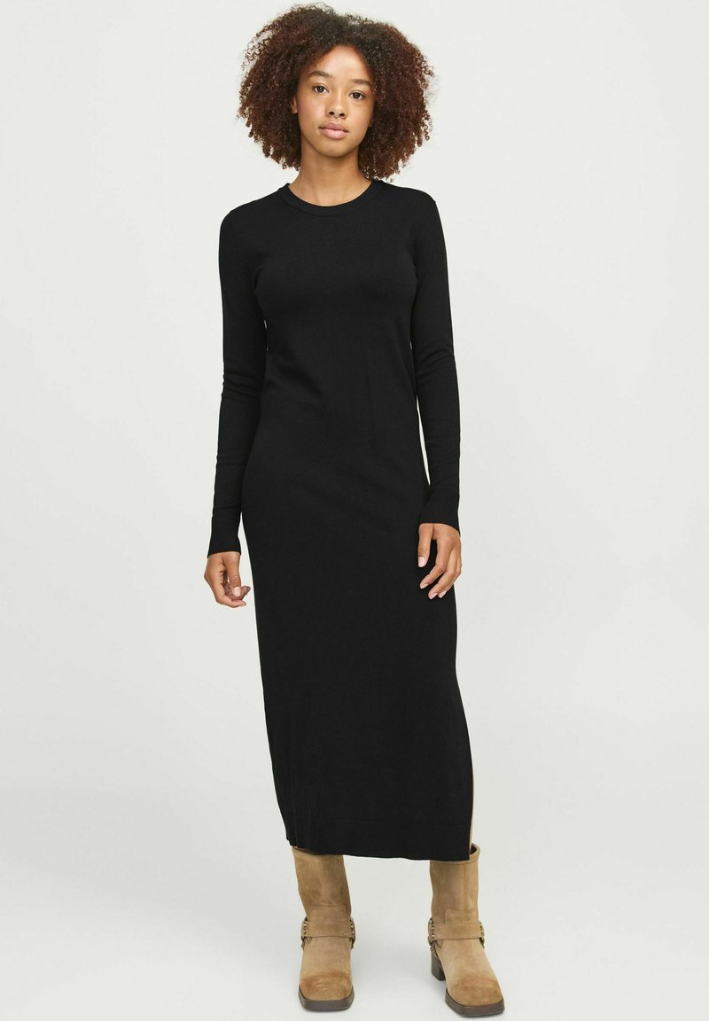 Vestido negro de manga larga con silueta ajustada, hecho de material suave. Dobladillo recto y cuello redondo. Llevado con botas de tobillo en color beige.