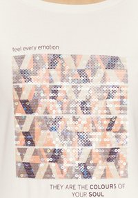 Weißes T-Shirt mit einem rechteckigen Design aus Pailletten in verschiedenen Rosatönen, Silber und Creme mit dem Text: "fühle jede Emotion" und "DAS SIND DIE FARBEN DEINES SEELES."