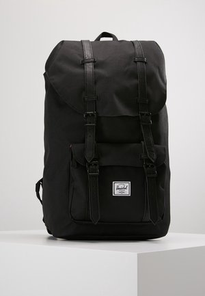 Zaino nero con esterno in tessuto, chiusura a patta, due spallacci in pelle regolabili e un piccolo logo sulla parte anteriore. Finitura texturizzata.