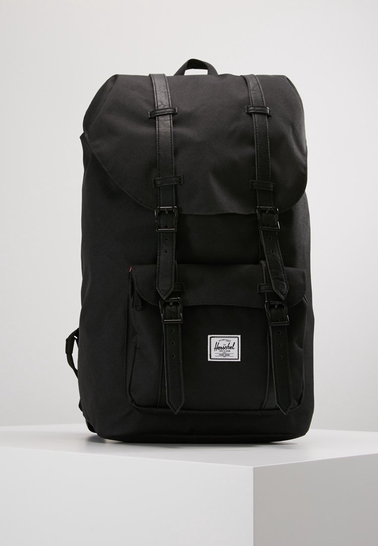 Czarny plecak o materiałowym wyglądzie, z klapą, dwiema regulowanymi skórzanymi ramiączkami i małym logo na przedniej łatce. Teksturowane wykończenie.