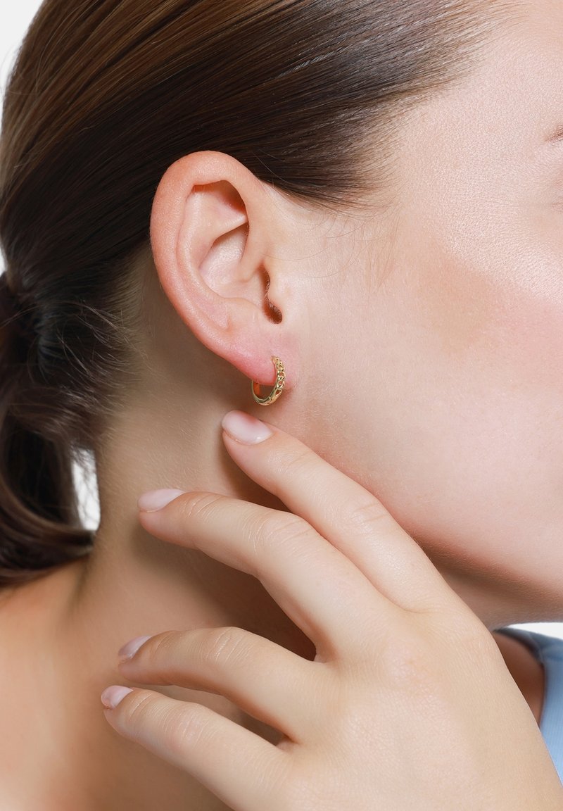 Boucles d'oreilles en or en forme de créoles avec un design en chaîne texturée, présentées sur l'oreille d'un modèle, mettant en valeur une surface lisse et une finition polie.