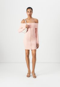 Off-shoulder strikket kjole i lys rosa med ribbestruktur, tettsittende fasong, frontglidelås, kombinert med en liten hvit veske og sandaler.