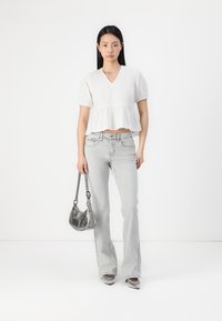 Fehér, rövid ujjú peplum blúz világosszürke, trapéz szabású farmernadrággal párosítva. A model egy apró ezüst színű táskát tart, és hegyes orrú ezüst cipőt visel.