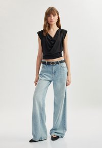 Top negro de tela caída con mangas cortas, combinado con jeans de pierna ancha de color azul claro y un cinturón negro con hebilla plateada circular. Se llevan zapatillas negras.