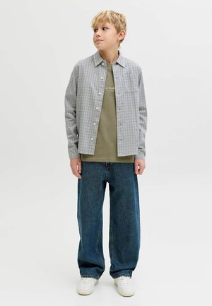 Camisa de algodón a cuadros sobre una camiseta verde oliva, combinada con pantalones vaqueros azules sueltos y zapatillas blancas.