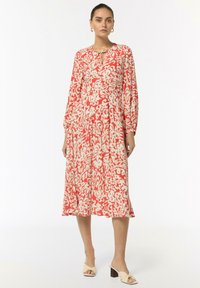 Rotes und cremefarbenes Blumendruckkleid mit langen Ärmeln, einem Schlüssellochausschnitt und einem fließenden Rock; kombiniert mit hellen, mit Absätzen versehenen Mules.