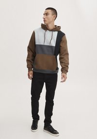 Hooded sweatshirt met een kleurblokontwerp in grijs, blauw en bruin, voorzien van een voorkantzak, gecombineerd met zwarte slim-fit broek en sneakers.