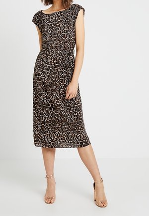 Femme portant une robe léopard mi-longue avec des manches courtes et une ceinture à la taille, assortie à des sandales à talons hauts nude avec bride à la cheville.