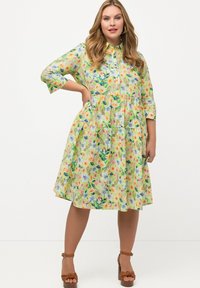 Vestido de botón con estampado floral en colores pasteles suaves, diseño en capas, mangas de tres cuartos, hecho de tela ligera. Tacones marrones con tiras.