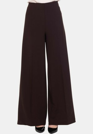 Pantaloni neri a gamba larga a vita alta indossati con tacchi a punta neri, mostrati dalla vita ai piedi su uno sfondo bianco.