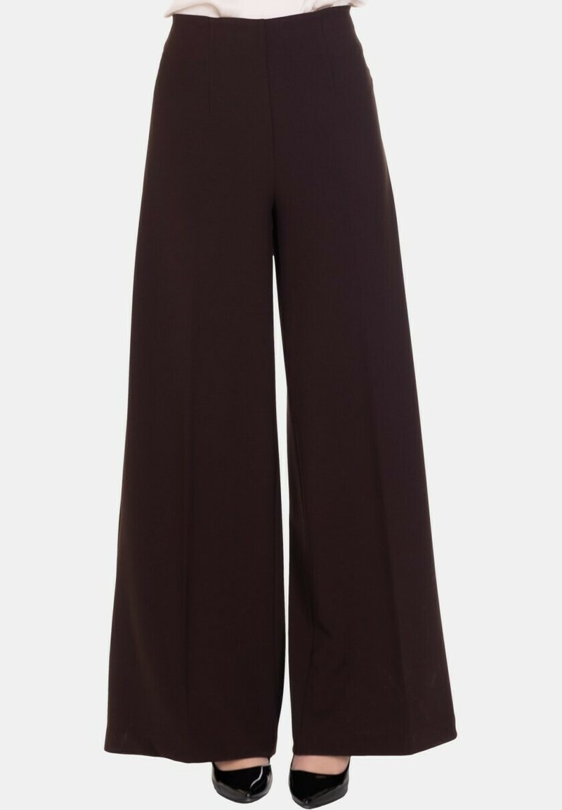 Pantaloni neri a gamba larga a vita alta indossati con tacchi a punta neri, mostrati dalla vita ai piedi su uno sfondo bianco.