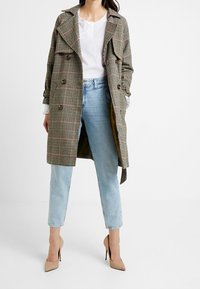 Manteau trench à carreaux dans des tons de brun et de beige, en tissu léger, avec un design croisé, accentué de grands boutons et de poches profondes.