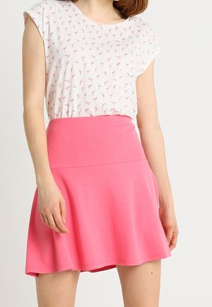Kvinde iført en hvid T-shirt med små lyserøde flamingo-prints, stoppet ned i et knaldrosa A-formet skørt.