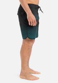 Herre svømmeshorts i svart og teal gradient. Har snor i livet, sidelommer, og et teksturert stoff med et stripete mønster.