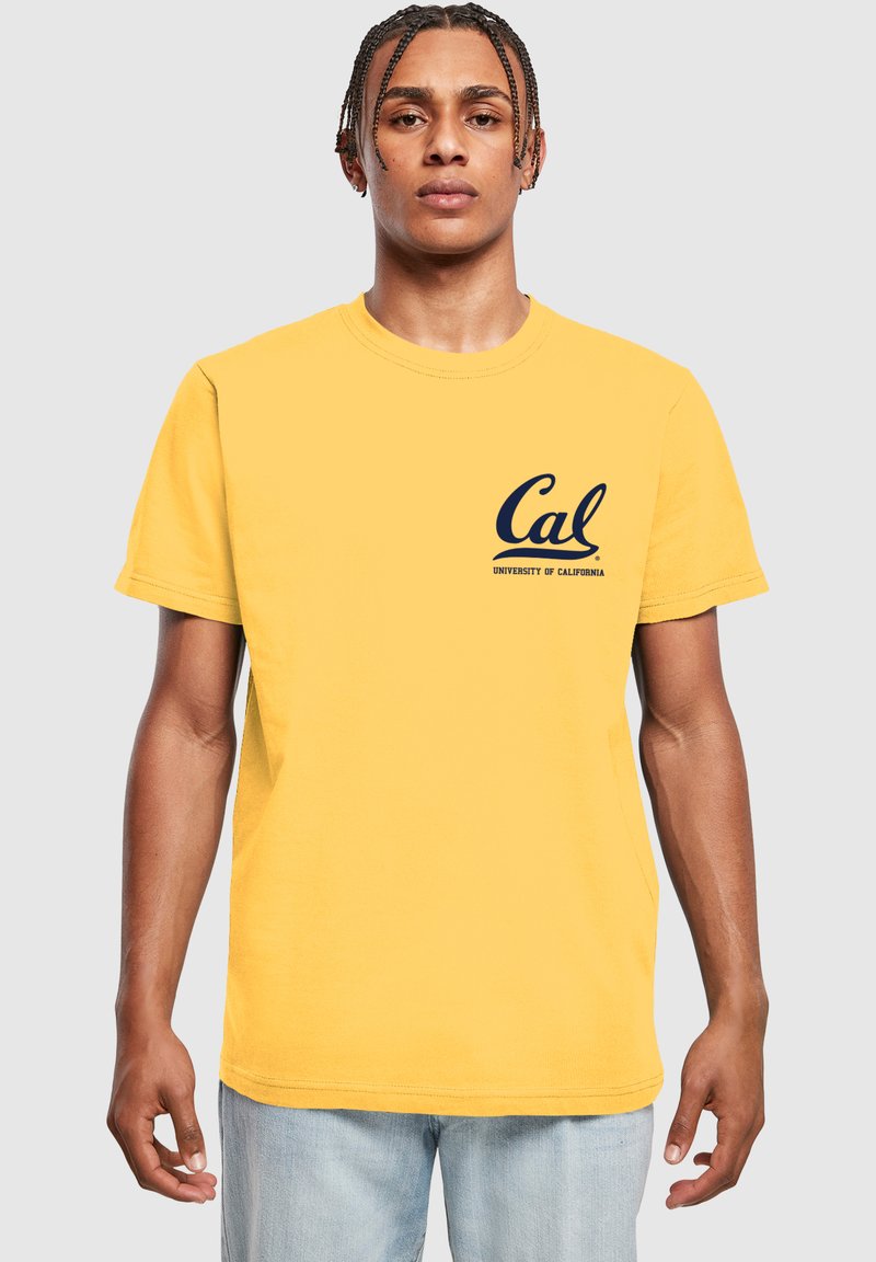 Žluté tričko s krátkým rukávem a kulatým výstřihem, které je zdobeno námořnickým logem s nápisy "Cal" a "University of California" na levé straně hrudníku.