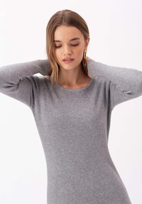 Szary sweter z prążkowanym splotem, z długimi rękawami i okrągłym dekoltem. Gładka tekstura, dopasowany krój, z subtelnymi detalami szycia.