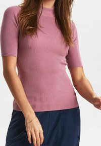 Rosa ribbad stickad tröja med hög hals och korta ärmar. Texturerad, figurnära design, slätt tyg. Matchad med mörkblå byxor.