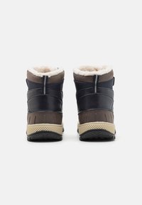 Un par de botas de invierno marrones y azul marino con suelas beige y forro de lana blanca, vistas desde atrás sobre un fondo blanco.