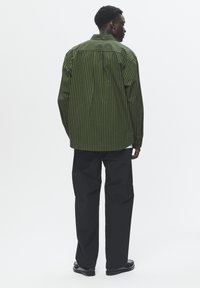 Groene en zwarte gestreepte shirt met een relaxte pasvorm, lange mouwen en een afgeronde zoom. Gepaard met zwarte broek en zwarte schoenen.