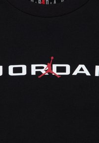 Μαύρο βαμβακερό t-shirt με εμφανές λευκό λογότυπο "JORDAN" και κόκκινη σιλουέτα παίκτη σε άλμα.
