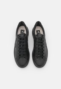 Musta nahkakengät, joissa on sileä pinta, pyöreä kärki, tasaiset nauhat ja logo pohjallisessa. Minimalistinen muotoilu.